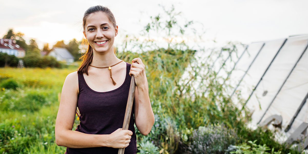 Frau mit Hacke in der Hand vor einem Feld